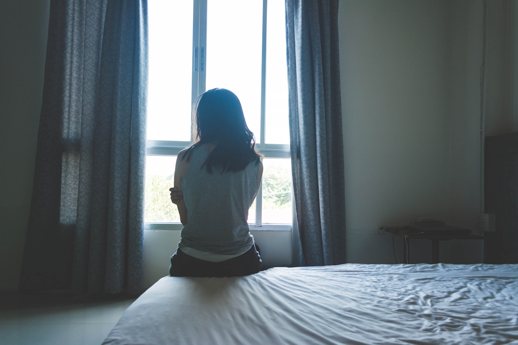 Woman sitting on bed in room with light from window